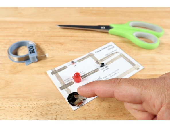 Measure, cut, peel, and stick Maker Tape path J. This path should cross over the end of path I, extend left and be stuck to the top of the battery. Your circuit is now complete!