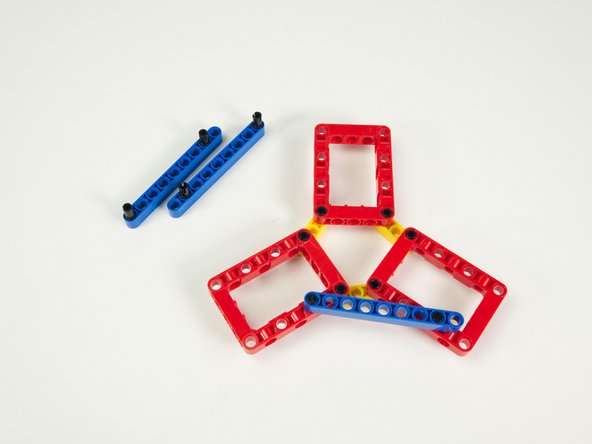 The pin at the end of the blue beam goes into the hole in the red frame next to the pin on the yellow beam located towards the center of the frame...