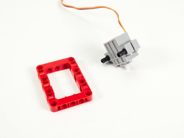 Attach the servo to the red frame using the black pins we just added, centering it so the pins and holes align.