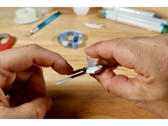 To keep the orientation clear, we will connect one LED leg at a time starting with the LONG leg. Bend that leg outward. Then measure, cut, peel, and stick a piece of Maker Tape to the top side of the leg as shown.