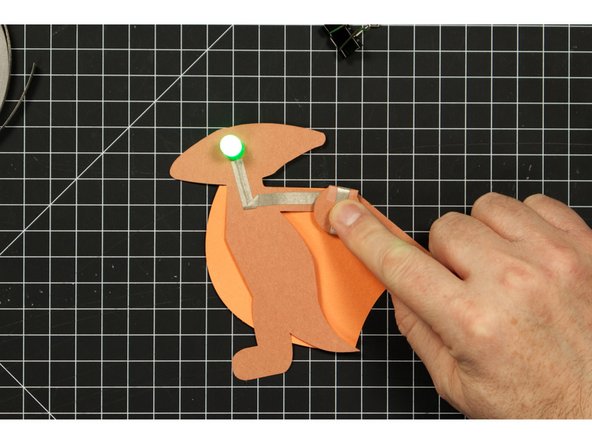 Fold down the round battery holder section on the back so that the positive line of tape make contact with the top of the battery.