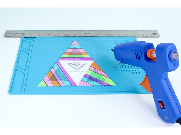 Use a hot glue gun to place hot glue on the inside of a frame while pressing one of the colored triangles into place on top. Be sure to be accurate with your placement as each edge of a given face will eventually need to be fastened to the next. Overhang can make this tricky.  Do this ONE FACE AT A TIME. 