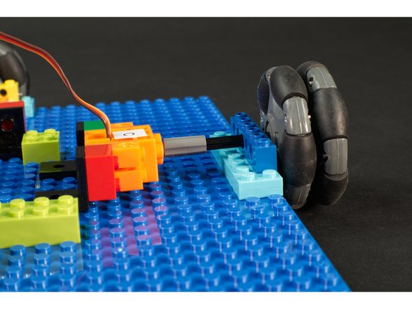 The shaft of the servo has a LEGO axle connector attached, and then a LEGO Axle connected to it and the omni wheel. It goes through a Technic brick with holes sitting atop a stack of two LEGO plates.