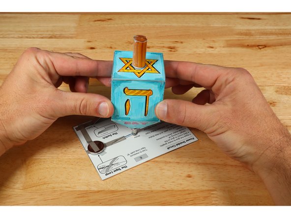 Use the small circle on the lowest part of the dreidel shape indicated for &quot;motor&quot; as the target while you press and hold the dreidel atop the hot glue. Hold until the glue sets. The more on-target and plumb (straight up and down) this placement is, the more &quot;true/evenly&quot; the weight of the dreidel shape will spin.