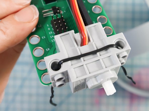 Use a plastic-covered twist tie to attach the servo motor through the GND and 3V holes.