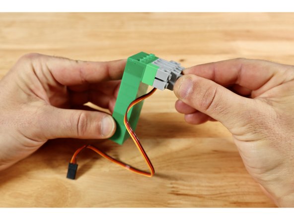 Connect the single (1x2) brick to either of the two recessed areas on the servo then connect the servo to the (2x4) cluster outward-facing studs on the tower. This orients the servo axle in the correct way to interact with the long straight gear that will eventually move your leprechaun upward.