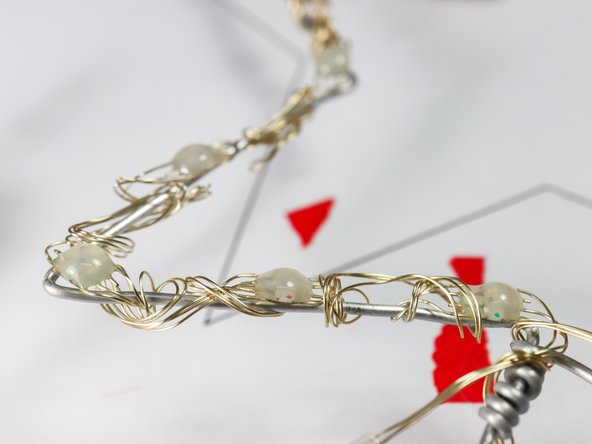 Carefully place each NeoPixel pixel around the star on every point, inner bend, and one in between on each starburst as shown. Wrap the excess wire around the sculpture wire to secure it.