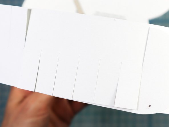 Tape the headband pieces to the sides of the paper as shown. One side's fringe will face up and the other will face down so that you can interlock them as shown.