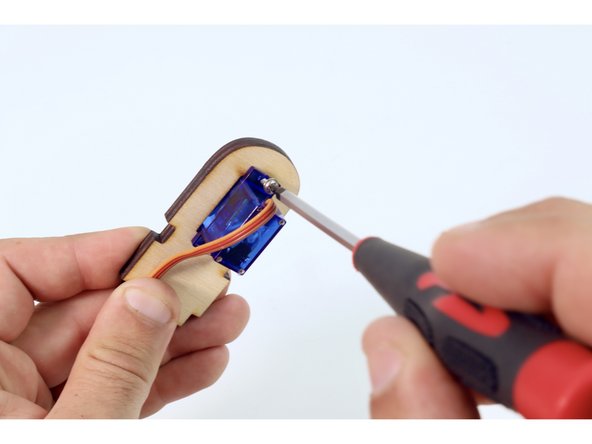 Using the wooden servo plate shown, and the two matching small screws found in the last servo bag, mount the remaining servo  using your Phillips head screwdriver.