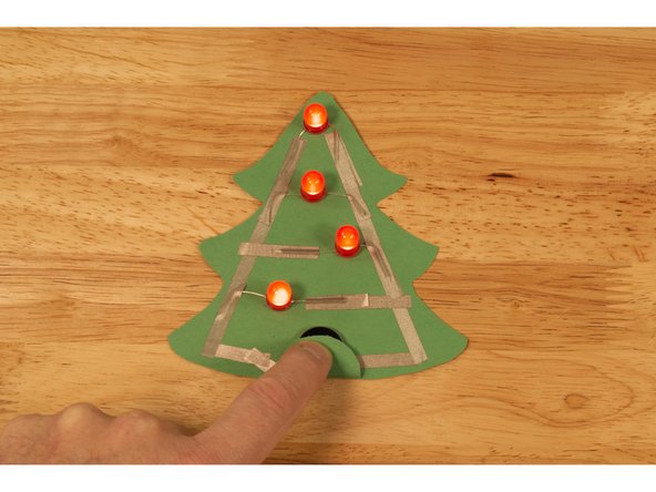 Place a battery in your circuit so that the negative side is touching the tape that leads to the right side of the tree.