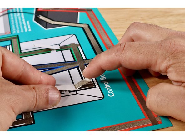 Install the switch by positioning it atop the gap (Maker Tape side down) where shown and securing it with another piece of Maker Tape. The fold should be atop the black horizontal line of the box graphic. The LED will now momentarily light up when the lever is pressed into contact with the upper part of the path across the gap.