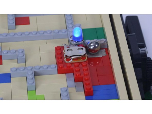 Since the steel ball is conductive we are using it to make contact between two pieces of Maker Tape to complete a simple circuit with an LED and a battery to indicate we've solved the maze.