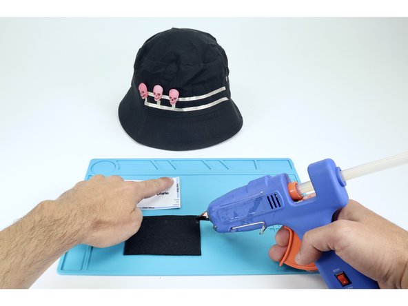Arrange yourself so you can stretch the hat over your knee with the area you want to make the &quot;back&quot; of the hat facing up at you. You should also be near enough to the hot glue gun to operate it safely.