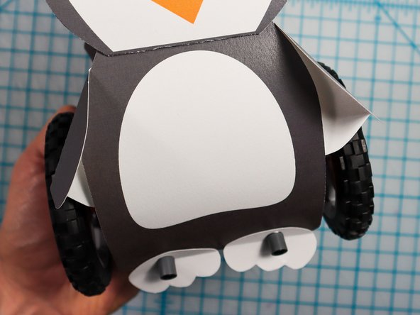 Thread the wings behind the penguin's body and squeeze the spot with the tape/glue to keep them in place.