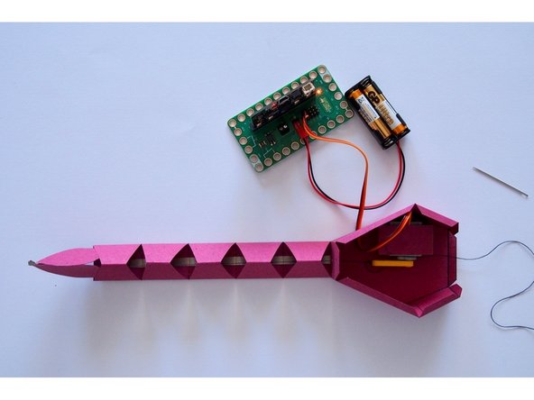 Tie the string to the end of the LEGO Beam in such a way that it is lightly tensioned when the mount faces towards the tail, and tight enough to pull the tail up when the beam points away from the tail.