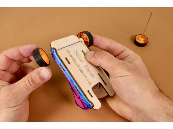 Take one of the two axle rod/wheel combos and thread it through the two drop-down holes located at the flat end of the chassis. Seat the third wheel onto the end of that same axle. This is the front end of the Solar Racer.