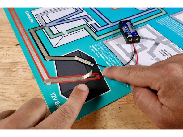 Cut two more small pieces of Maker Tape and use them to hold the red wire from the battery pack in contact with the red path and the black wire in contact with the black path.