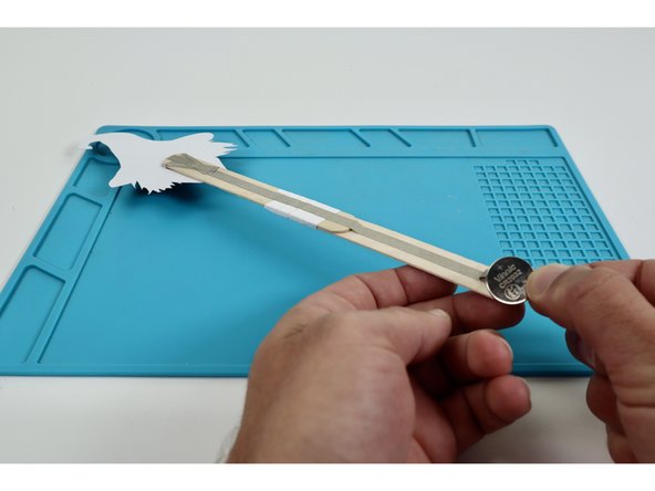 Begin the battery installation by sticking the CR2032 battery atop the tape loop with the positive (+) side facing UP.