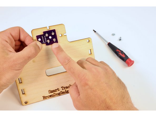 Position the circuit board as pictured so that the metal pins on the back drop through the rectangular hole on the wooden piece. This should allow the circuit board to lay flush against the wooden plate.