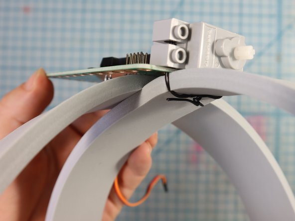 Use a plastic-covered twist tie to attach the servo motor through the GND and 3V holes.