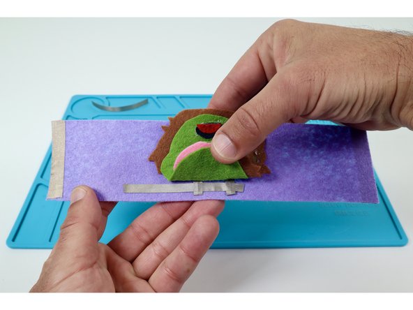 Lift up the edge of the felt design that hides the SHORTER LED legs  enough to reveal them.