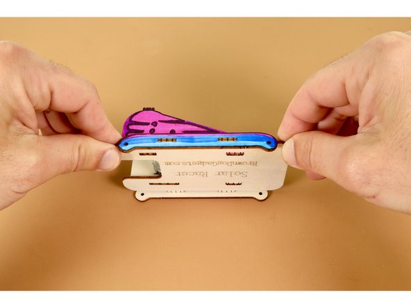 Pick up the partially-assembled chassis and orient it so that you are looking at the engraved underside while seated. Now press the two downward-facing  tabs on the chassis into the two slots of the long rounded end panel.  Repeat this EXACT process to seat the remaining matching body panel on the opposite side of the chassis.