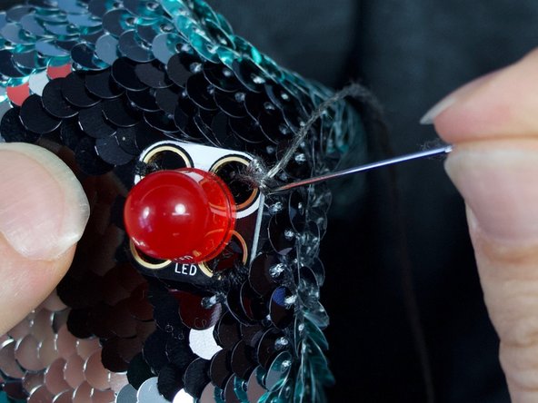 Sew a few finishing knots to the negative hole of the first red LED to make a good connection. End with the thread on the inside of the shirt. DO NOT cut the thread.