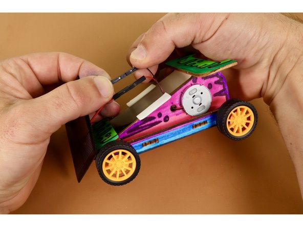 To attach the solar panel to the completed Solar Racer chassis, you will first need to peel and stick two pieces of the included double-sided foam tape where shown in photo two.