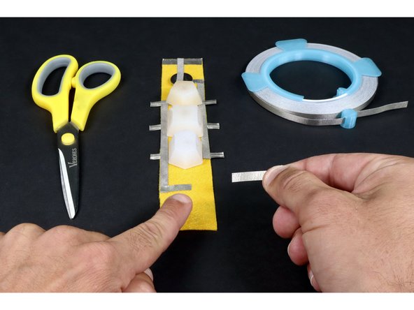 Measure cut peel and stick another longer piece of Maker Tap that reaches across/atop all three long LED legs and about 1/2&quot; beyond in the direction of the bracelet end without the battery.