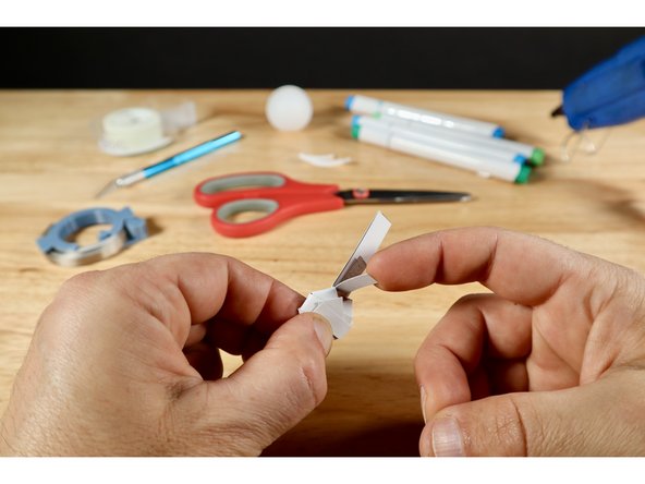 With your other hand, tuck the remaining free tab (that you cut from the template sheet) below the battery by path "C." and curl the other end up to the join the rest of the protective tabs. Pinch and hold with one hand.