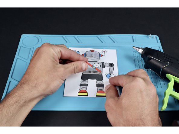 With the belt faced UP, lay the &quot;x&quot; side of one of the edge tabs in the glue and wait for the glue to cool. Note: Use a pencil or popsicle stick instead of your finger if you feel the need to press the tab into the glue.