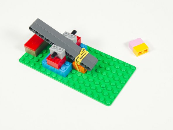 Wrap the Rubber Band around the beams so they get pulled down towards the brick.