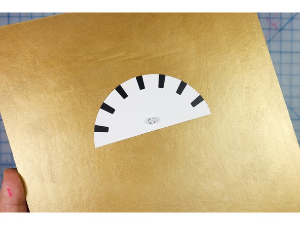 Insert the gauge face over the motorhead and glue it to the cardboard with hot glue.