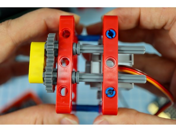 Get the frame piece with the motor attached and connect the two together as shown, with the blue pins on the bottom and the gray axles on the top.