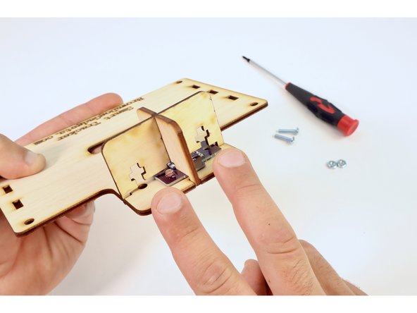 Press the crossed divider assembly in place atop the circuit board so that the pegs fit into the holes on the larger plate.