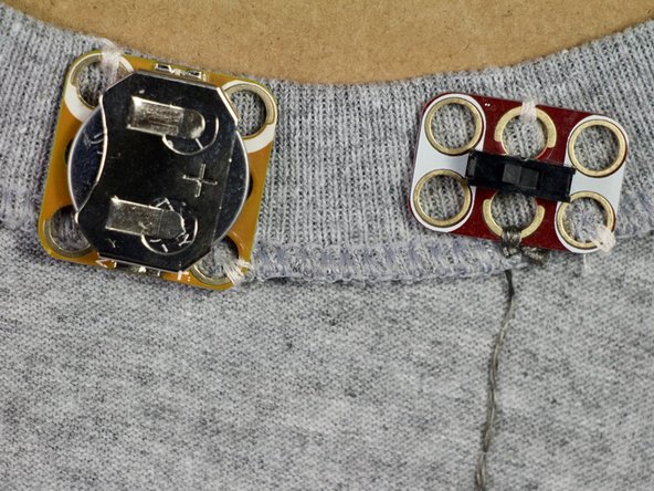 Load your needle with conductive thread. Start by making a few finishing knots around the middle bottom hole of the switch.