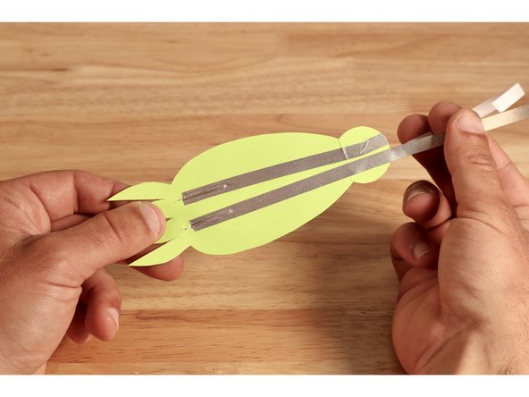 Flip shape over and make two more Maker Tape pathways for each of the legs on the opposite side. Lay the tape PAST the fold, over the tab and to the front side of the tab, leaving a gap between their ends and the ends of the first two paths you made.