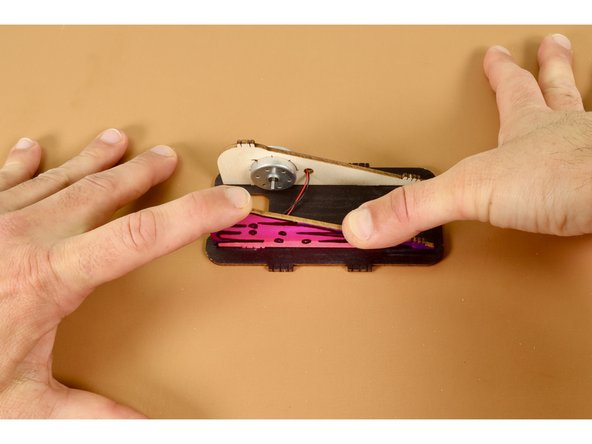 With the developing chassis still laying flat against the table find the remaining triangular body panel and press it into place; seating the two identical tabs into the two corresponding slots along the right edge of the base plate.