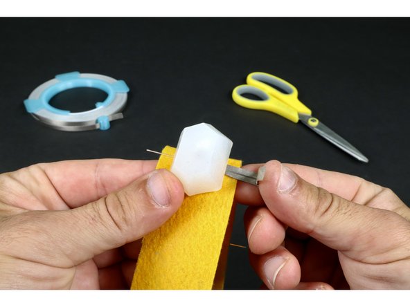 Use photo 2 as a reference and stick half of the length of the Maker Tape segment to the under side of one of the LED legs (this puts the sticky side up). Then fold the remaining half back over the top of the first half. The result should be that the LED leg is now sandwiched between Maker Tape.