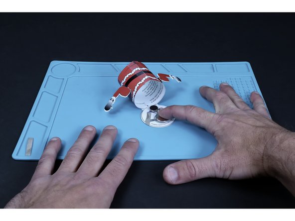 Press the battery atop that tape loop so that the positive (+) side faces UP.