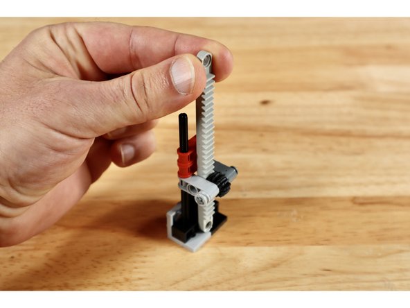 Insert the gear rack into the space behind the bevel gear so the teeth from both gears are facing one another and the smooth side of the gear rack is facing the 2 axle hole cross blocks behind it.