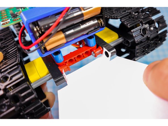 Use two pin/beam sets to connect the paper to the back of the tank under the battery pack where shown.