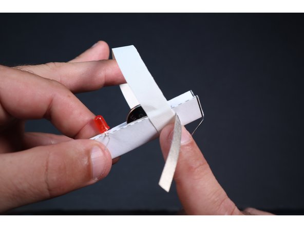 Pull the remaining LED leg and unsecured Maker Tape temporarily  out of the way. Start a Gaffer's/Duct tape section as shown and wrap it all the way around (even over top the secured LED leg) to cinch the sides into contact with the now hidden battery.