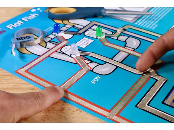 The next Maker Tape path must jump OVER the Green LED Path without touching it. Use extra length when measure to create the necessary slack to avoid contact with the path below.