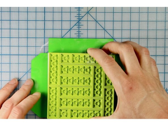 Place the lego structure in the center of the square and wrap the square flaps first, then wrap the ones with the tapered edge.