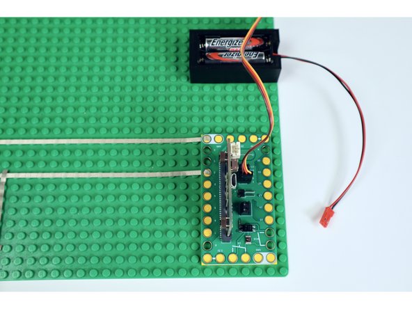 Add two AAA batteries to your battery holder and, with a big loop of duct tape or some hot glue, stick it into place on the baseplate below and to the right of the servo.