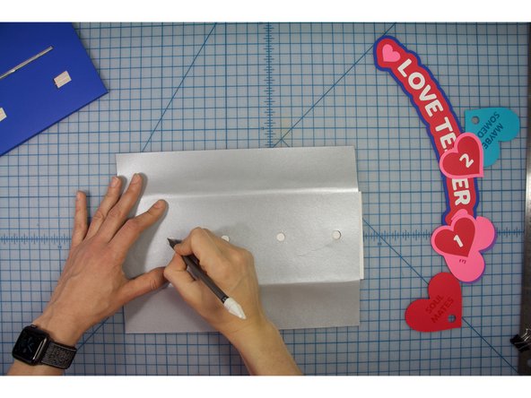 Align the silver piece with the base, centering the holes and wrapping the paper around the back of the tall piece.