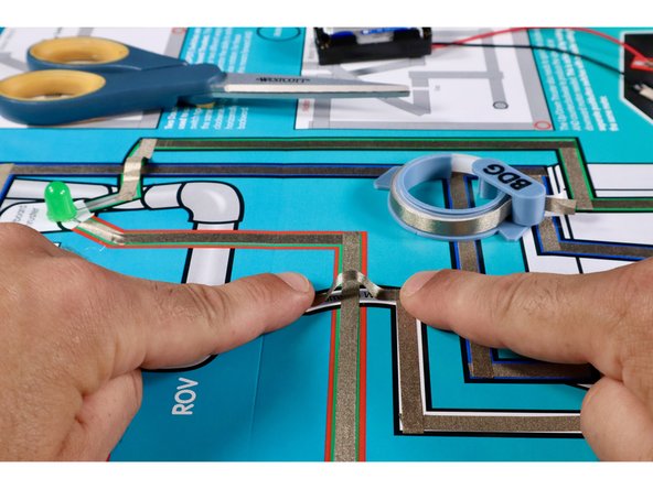 Measure, cut, peel, and stick the first two Maker Tape paths shown. They should lead from the Black Negative (-) Path coming out of the control box, up toward the White LED.