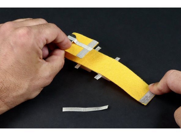 Peel and stick the two smaller pieces so that they overlap and are located  on the UNDERSIDE of the end opposite the battery.