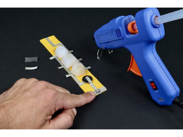Use a hot glue gun to make 2 small glue dots on opposite sides of the tape loop.